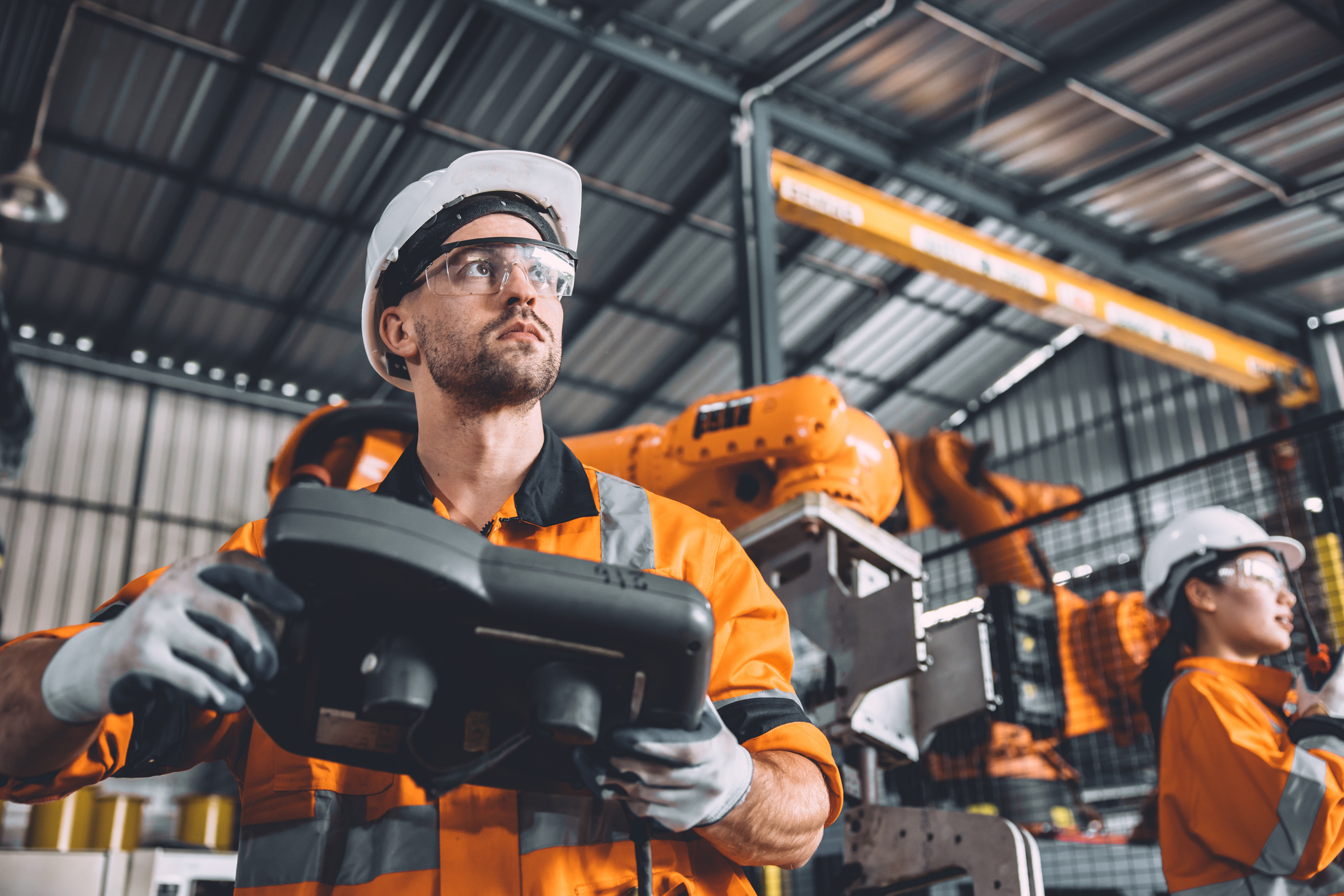 Engineer team working with robot welding in automation factory. People worker in safety suit control robotic arm in automated manufacturing industry technology.